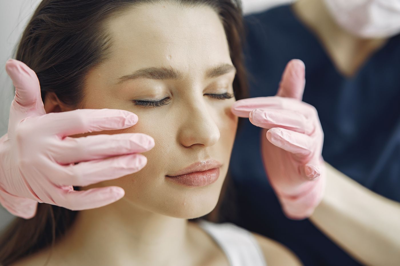A clinician wearing gloves gently examines the skin around a patient's closed eyes during an eyelid consultation
